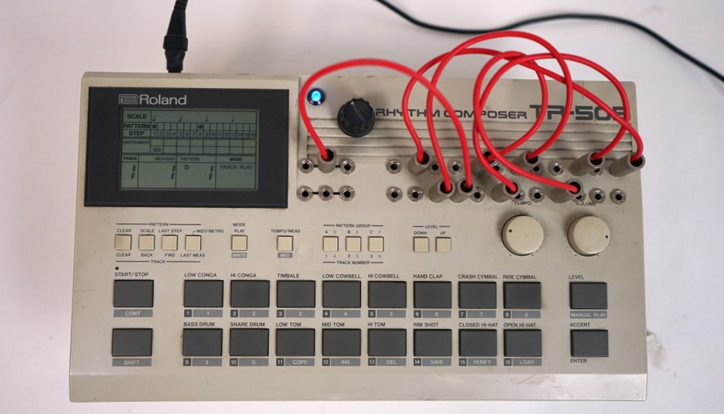 Modifizierte Roland TR-505 Drum Machine mit Circuit-Bending-Patchbay, roten Patchkabeln, LCD-Display und zusätzlichen Reglern.